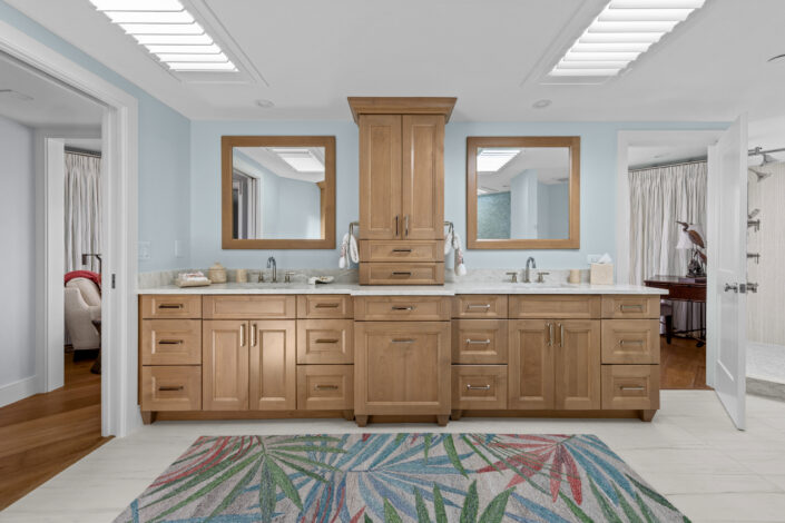 lands-end-penthouse-0S3A0135 Primary bath double vanity with wood cabinetry, framed mirrors and palm-leaf runner