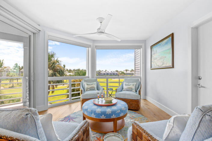 lands-end-penthouse-0S3A0317 Sitting area with round upholstered ottoman and woven swivel chairs overlooking palms and golf course