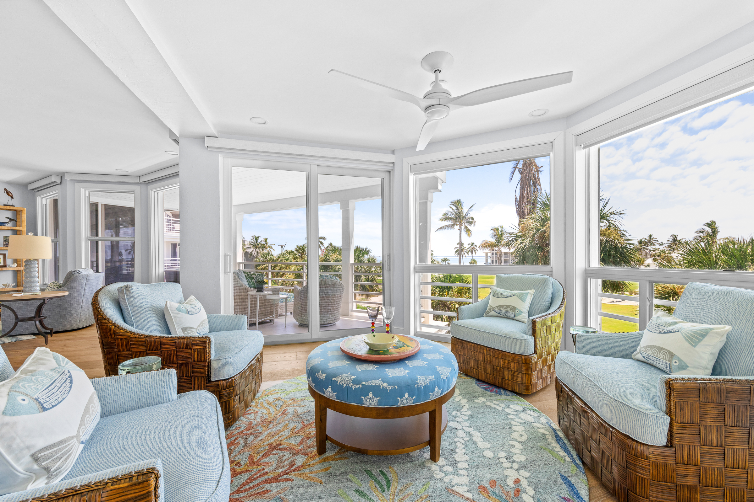 Captiva Island penthouse living room with wraparound windows, blue upholstered seating and palm views