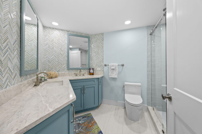 lands-end-penthouse-0S3A0357 Guest bath with chevron glass tile, blue vanity and frameless glass shower